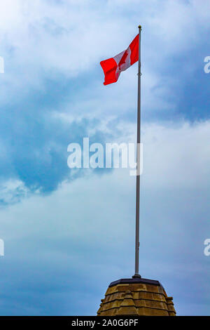 Un drapeau canadien sur un piédestal en pierre se dresse contre un ciel bleu nuageux. Banque D'Images
