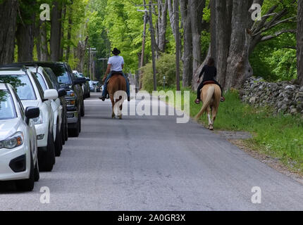 Un couple de l'équitation sur une paisible route de campagne pleine de voitures en stationnement sur l'épaule. Banque D'Images