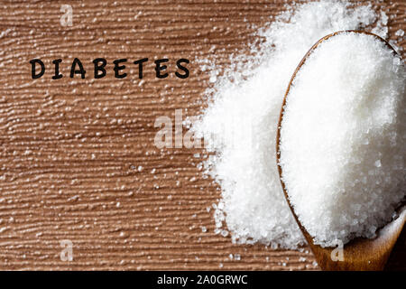 Le sucre dans une cuillère en bois sur la table en bois. Diabète mot écrit sur l'arrière-plan. Selective focus Banque D'Images