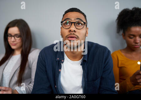 Inquiets young african american man attend son tour pour interview assis avec d'autres candidates Banque D'Images