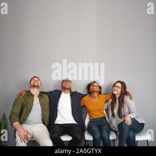 Groupe de jeunes amis multiraciale, assis sur une chaise avec les bras autour de l'épaule de l'un de l'autre s'amusant et à la recherche jusqu'à l'espace de copie Banque D'Images