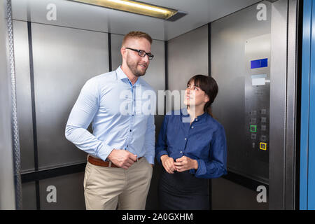 Vue latérale d'un businessman and Businesswoman Standing In ascenseur à parler les uns avec les autres Banque D'Images