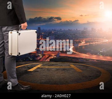 Business man with strong metal breifcase article sur l'atterrissage d'hélicoptère au-dessus du bâtiment toiture avec lever de soleil sur scène urbaine Banque D'Images