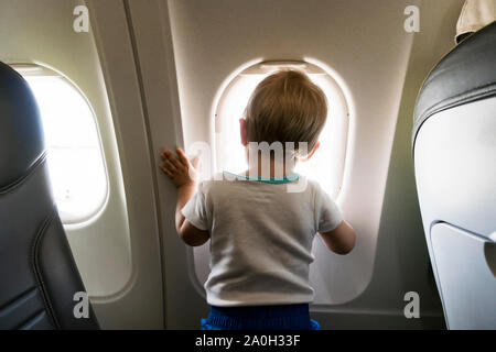 Un an bébé garçon par airplain curieusement à la fenêtre. Banque D'Images