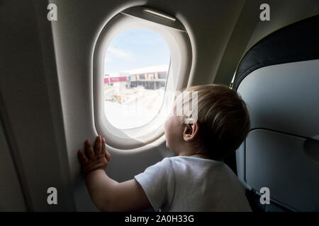 Un an bébé garçon par airplain curieusement à la fenêtre. Banque D'Images