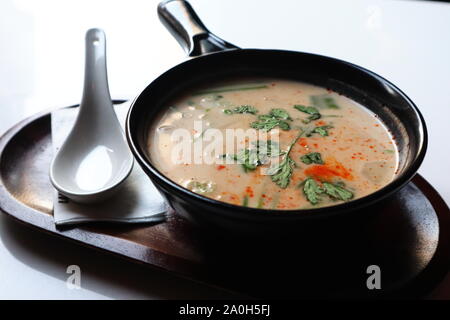 Soupe thaï à la noix de coco et de chaux sur bois plateau avec 1 cuillère à soupe traditionnelle sur fond blanc brillant Banque D'Images