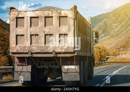 Vue arrière sur un grand camion benne se déplace sur une route dans les montagnes durant le transport de marchandises sur de longues distances. Livraison rapide par sol transportati Banque D'Images