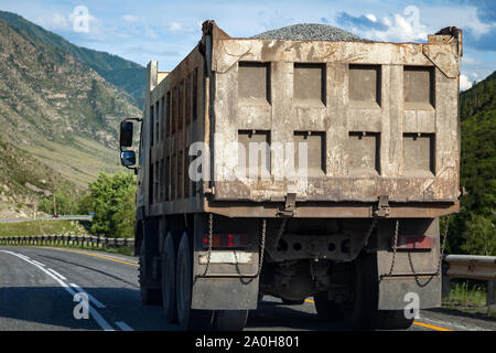 Vue arrière sur un grand camion benne se déplace sur une route dans les montagnes durant le transport de marchandises sur de longues distances. Livraison rapide par sol transportati Banque D'Images