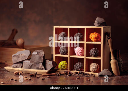 Bonbons de chocolat en boîte en bois. Morceaux de chocolat, des bâtons de cannelle, d'anis et les grains de café sur un fond brun. Banque D'Images