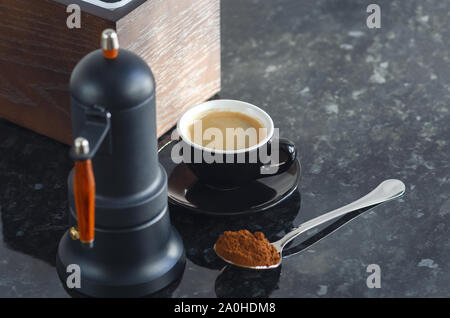 Type cafetière geyser et la tasse de café de couleur noire, avec des grains de café et du café fraîchement moulu dans une cuillère. Banque D'Images