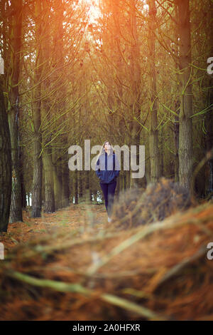 Jeune femme dans un imperméable randonnée par une forêt Banque D'Images