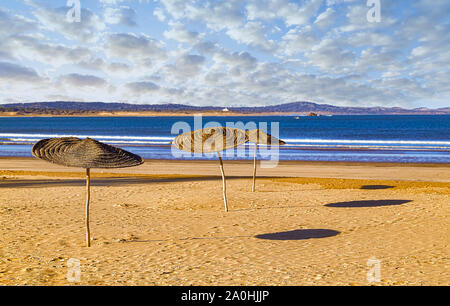 La lumière du matin sur la plage déserte d'Essaouria,un site du patrimoine mondial de l'Unesco au Maroc,parasols typiques fabriqués à partir de matériaux naturels. Banque D'Images