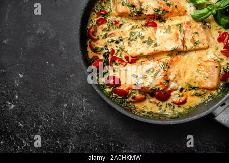 Close up de délicieuses spécialités toscanes saumon crème aux épinards et tomates cerises dans une casserole sur fond noir Banque D'Images