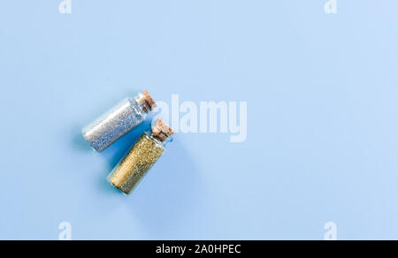 Deux bouteilles en verre d'argent et d'or glitter tinsels brillants sur fond bleu pastel. Concept de fête magique. Banque D'Images