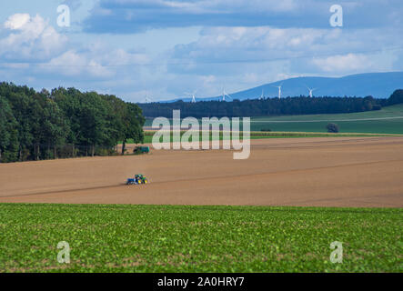Tracteur John Deere Seeding pour l'année prochaine sur le champ vide en zone rurale avec les éoliennes dans la distance Banque D'Images