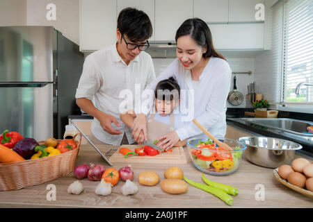 L'enseignement de sa fille mère asiatique salade de légumes râpés avec père debout sur le côté tandis que la famille était la cuisson dans la cuisine à la maison. Fami Banque D'Images