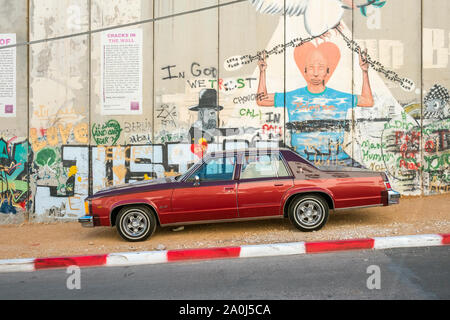 La Palestine, Cisjordanie, Bethléem. Oldsmobile Delta 88 vintage voiture en face d'une partie de la barrière de Cisjordanie Israël mur recouvert de graffitis. Banque D'Images