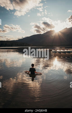 Teenage boy standing dans un lac à la recherche de soleil sur une montagne. Banque D'Images