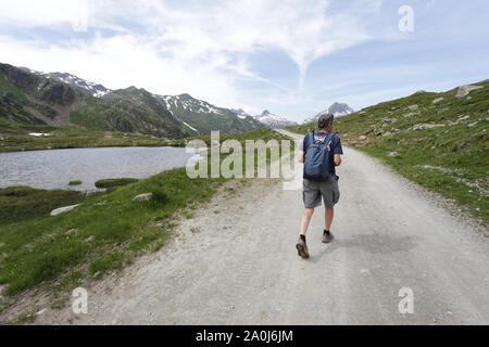 Un homme avec un sac à dos à marcher le long d'une route de gravier dans les Alpes suisses. Banque D'Images