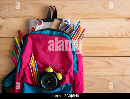 Sac à dos pour l'école avec des fournitures scolaires et de l'horloge sur fond de table en bois. Concept Retour à l'école. Banque D'Images