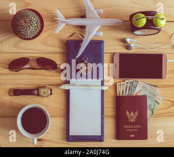Vue de dessus de l'ordinateur portable, un stylo, lunettes, tasse de café, passeport, argent, téléphone portable, écouteurs, montre-bracelet, cactus, réveil, avion et boussole sur sol en bois Banque D'Images