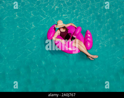 Vue de dessus de femme flottant sur flamant rose gonflable dans une piscine. Banque D'Images