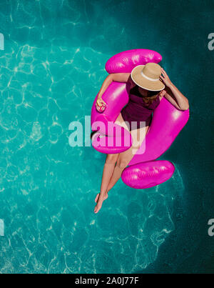 Vue de dessus de femme flottant sur flamant rose gonflable dans une piscine. Banque D'Images
