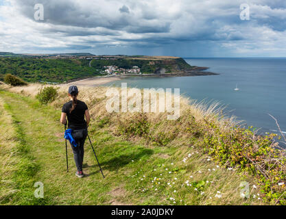 Vue arrière du female hiker sur le chemin côtier de Cleveland Way avec storm clouds over Runswick Bay dans la distance. North Yorkshire, Angleterre. UK Banque D'Images