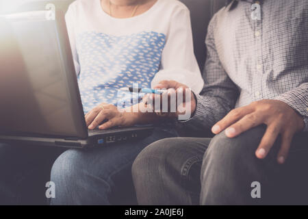 Compagnon de l'homme et la femme dans une tenue décontractée de discuter pendant l'utilisation d'ordinateur portable et assis sur un canapé dans le bureau. Banque D'Images