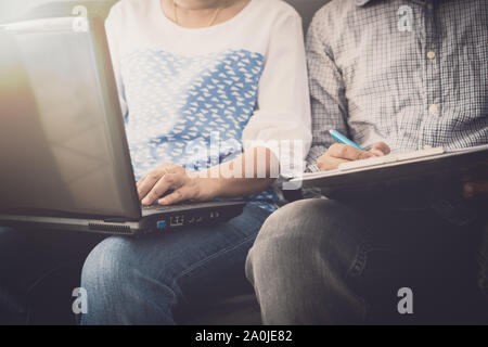 Compagnon de l'homme et la femme dans une tenue décontractée de discuter pendant l'utilisation d'ordinateur portable et assis sur un canapé dans le bureau. Banque D'Images