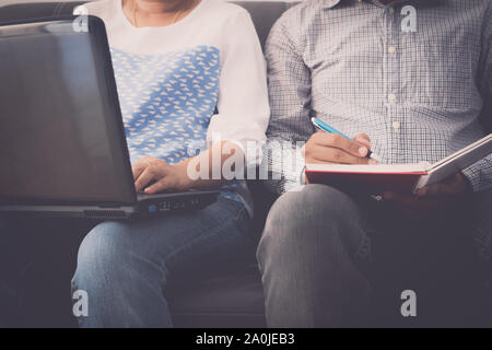 Compagnon de l'homme et la femme travaillent ensemble sur l'ordinateur portable et le bloc-notes sont assis sur un canapé dans le bureau. Banque D'Images