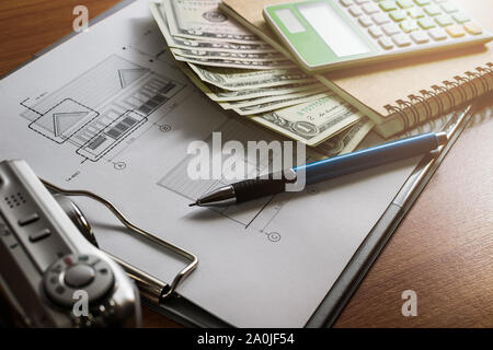L'investissement pour la construction avec le budget, plan de construction, stylo, argent, ordinateur portable, appareil photo et une calculatrice sur table en bois Banque D'Images