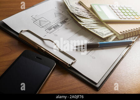 L'investissement pour la construction avec le budget, plan de construction, stylo, argent, ordinateur portable, téléphone intelligent et calculateur sur table en bois Banque D'Images