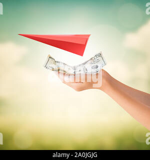 Hands holding US Dollars remarque pour le paiement avec l'origami avion rouge sur fond d'été Banque D'Images