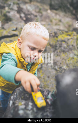 Bébé Garçon jouant avec des jouets sur un rocher. Petit enfant marche sur les montagnes rocheuses. Banque D'Images