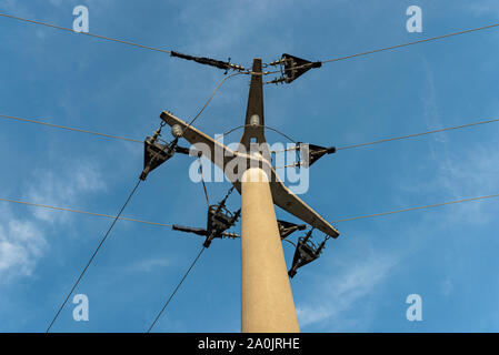 Poteau électrique en béton avec isolateurs en céramique et les lignes de tension en arrière-plan, ciel bleu avec des nuages blancs. Banque D'Images