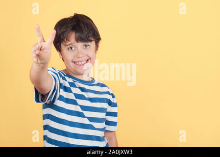 Sourire de l'enfant faisant la victoire.numéro deux sur fond jaune Banque D'Images