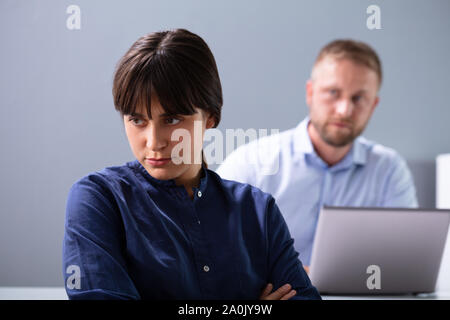 Angry Businesswoman Sitting in front of Businessman With Laptop à contre fond gris Banque D'Images