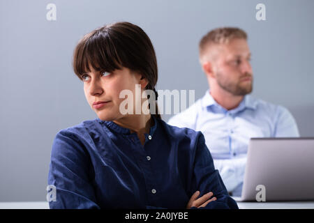 Angry Businesswoman Sitting in front of Stressed Businessman à contre fond gris Banque D'Images