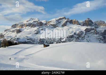 Regardez quand le soleil est bas sur un paysage hivernal enneigé avec une hutte en bois, le Groupe Sella en arrière-plan et un ciel bleu. Banque D'Images