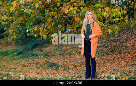 L'heure du coucher du soleil à pied femme. Tenues décontractées confortable pour la fin de l'automne. L'ambiance chaleureuse et confortable. Adorable petite fille blonde posing in outfit chaleureux et cosy de l'automne nature fond flou. Création pour agréable fin de semaine. Banque D'Images