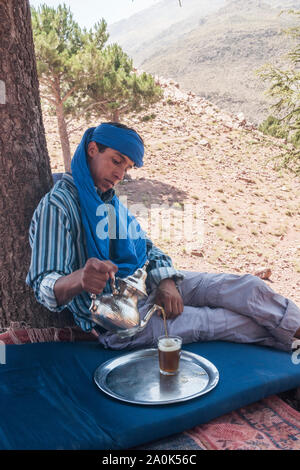 Homme marocain dans la vingtaine s'arrête pour se reposer et se verse un verre de thé à la menthe d'une théière d'argent sous un arbre à Tizi 'n Tamer, 2200 mètres de haut en Banque D'Images