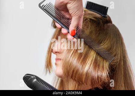 Coiffeur professionnel crêper les cheveux bruns longs avec des fers de cheveux au salon de beauté. Close-up Banque D'Images