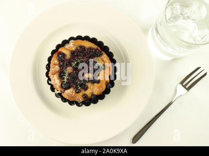 Chiacciata "all'uva' dans une assiette blanche, verre d'eau, de la fourchette. Sweet toscane typique focaccia avec de la pâte à pain, huile, sucre, raisin noir.fond blanc Banque D'Images