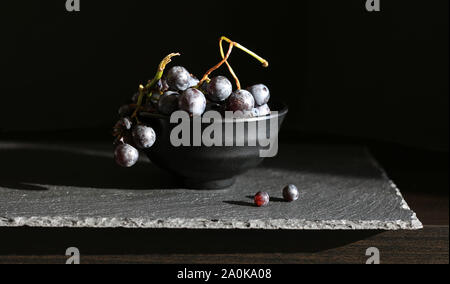 Le raisin noir frais dans une tasse noire isolé sur fond sombre Banque D'Images