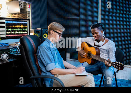 Deux jeunes hommes qui travaillent plus multiculturelle nouvelle chanson en studio d'enregistrement sonore Banque D'Images