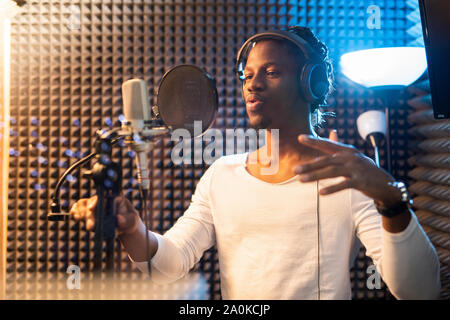 Jeune homme africain en t-shirt blanc et écouteurs interprétant des chansons en studio Banque D'Images