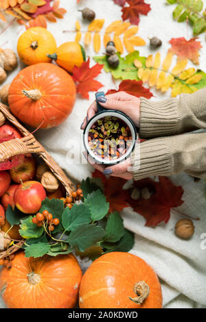 Girl holding du thé chaud avec des herbes entre les citrouilles et les pommes mûres, les feuilles d'automne Banque D'Images