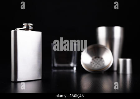 Shaker en métal, hip flask et verre de vodka. Accessoires Barman sur la table. Fond noir. Banque D'Images