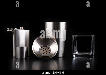 Shaker en métal, hip flask et verre de vodka. Accessoires Barman sur la table. Fond noir. Banque D'Images